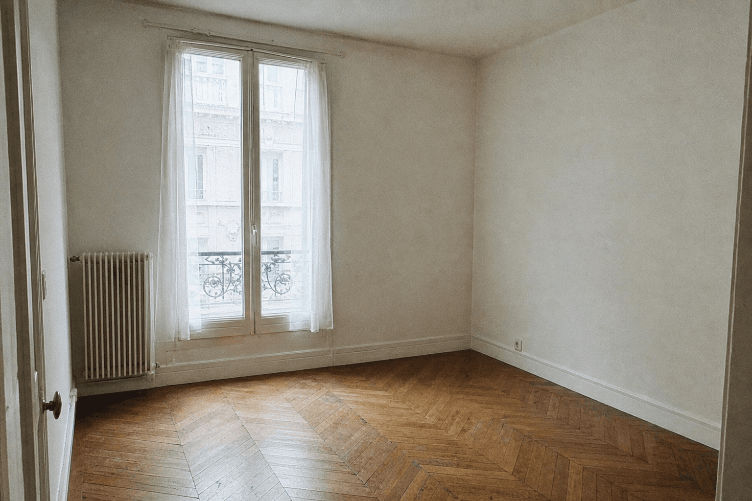 Studio parisien vide, parquet en point de Hongrie, une fenêtre